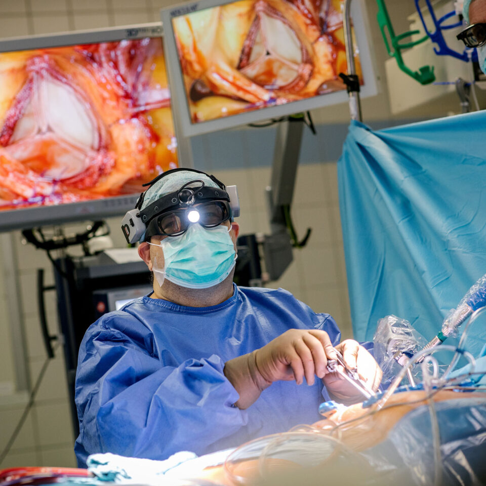 Prof Bakhtiary bei einer minimal-inasiven Herzklappen-OP, bei der er zu Beginn der OP eine 3D-Kamera in den Brustraum und ins Herz schiebt und dann die ganze OP auf den großen Screens im OP-Saal verfolgt. Die beiden Monitore hinter ihm sind die Screens, auf denen der zweite Operateur die OP sehen kann